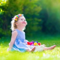cute baby girl sitting on grass with easter eggs in basket