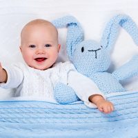 cute baby boy lying in bed with bunny toy and blue blanket