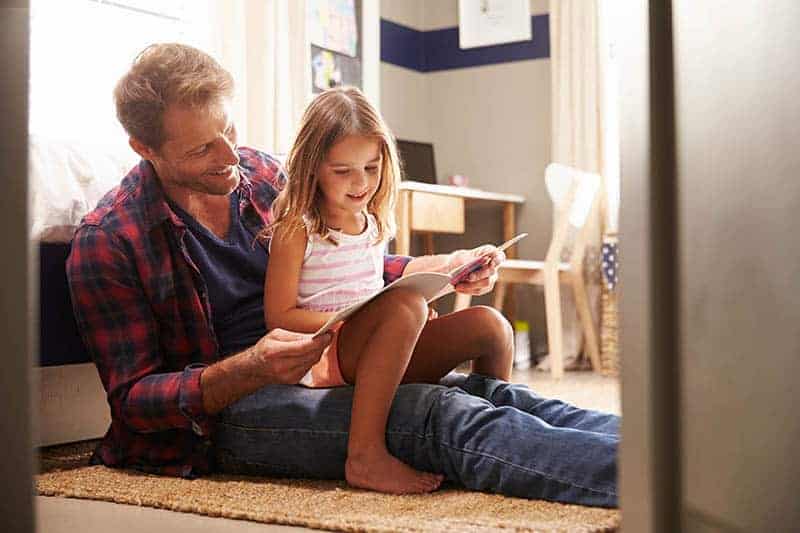 father reading a book with his daughter in bedroom