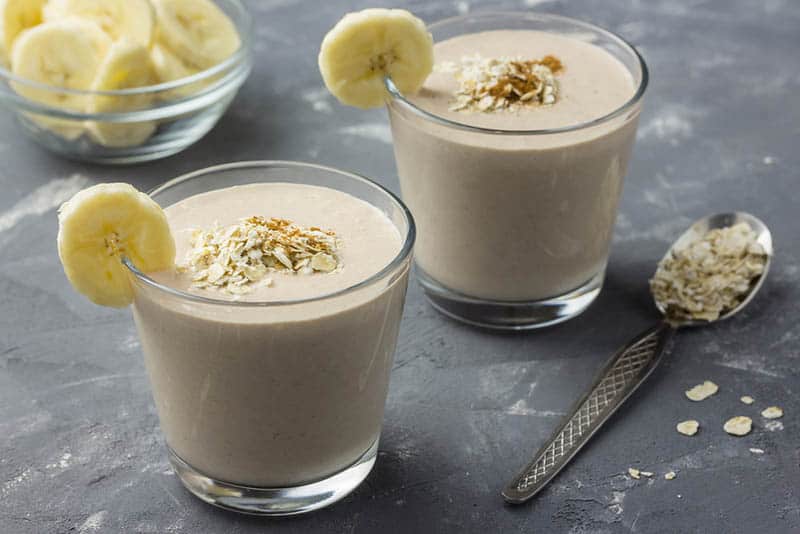 fresh banana, coconut and oat smoothie with spoon with oats on the table