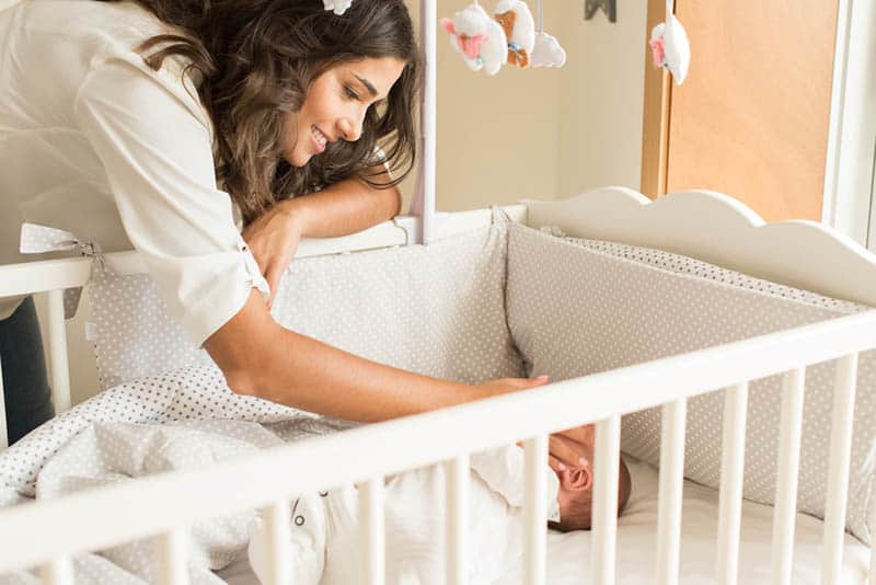 happy mother placing baby to sleep in crib