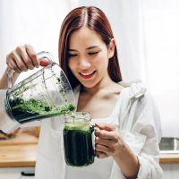 smiling woman putting green smoothie in the glass