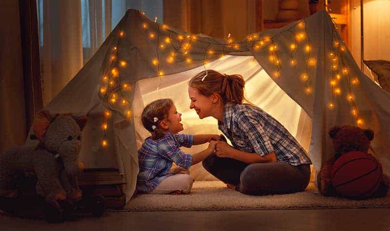 mother and daughter sitting in a tent at home and having fun