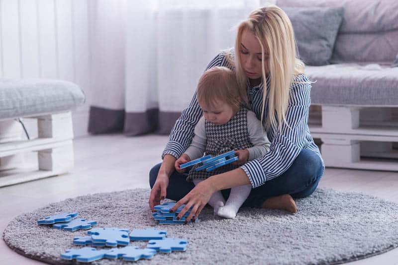 mother playing puzzles with baby girl on the floor 