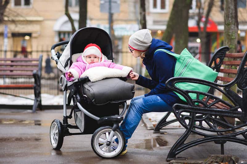 mother sitting on the bench with baby in a stroller
