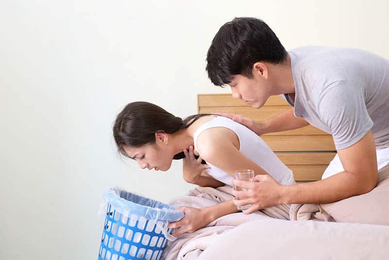 pregnant woman feel sick on bed in the room and husband holding a glass of water