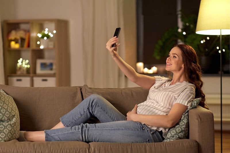 smiling pregnant woman lying on the couch and taking a selfie