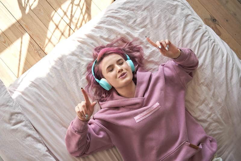 teenager girl with pink hair listening to music on the bed