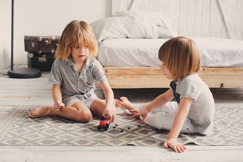 two happy siblings playing with toy cars at home in the morning