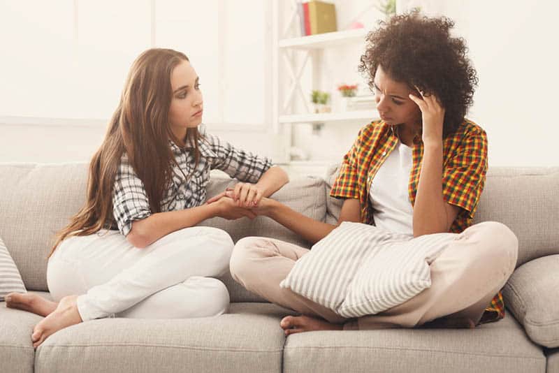 woman comforting her sad friend on the couch
