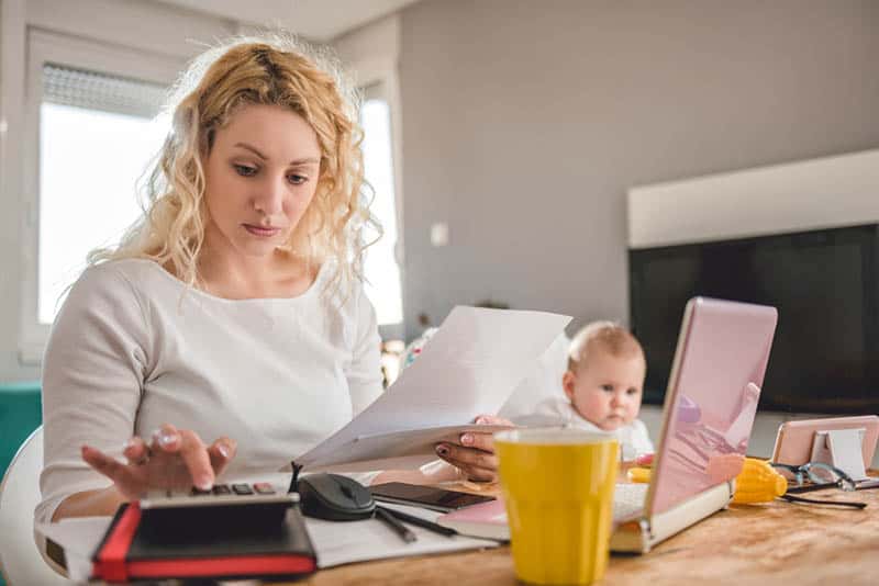 worried young mother checking bills and financy with baby in chair