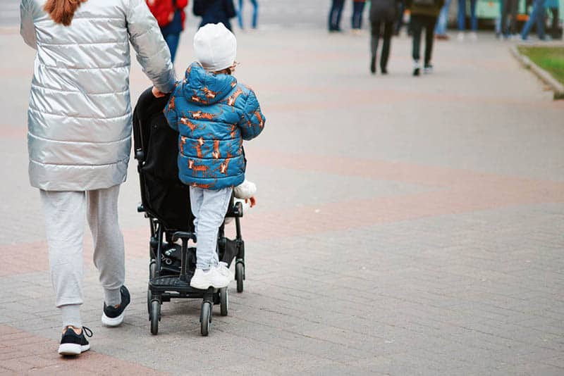 young mother walking with her son driving on a stroller