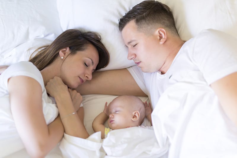 young parents sleeping in bed with their baby in the middle