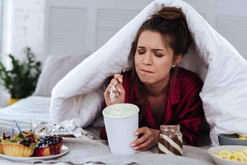 young pregnant woman eating different types of food in bed