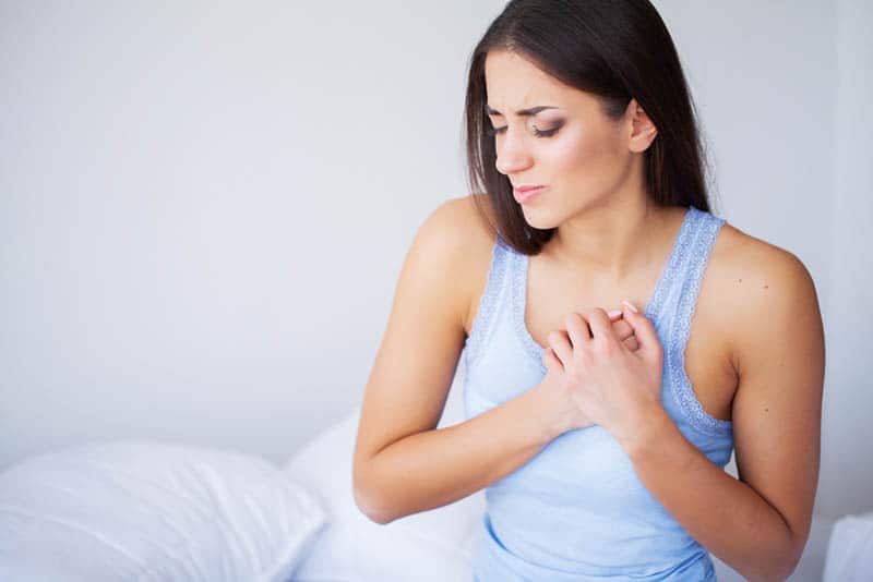young woman sitting on the bed and feeling pain in breasts