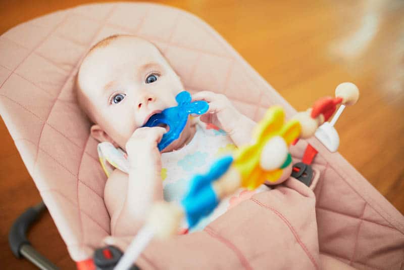 Adorable baby girl sitting in bouncer and playing with colorful toys
