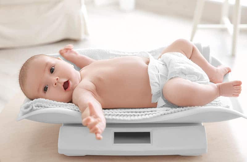 adorable baby boy wearing diaper and lying on the scale at home