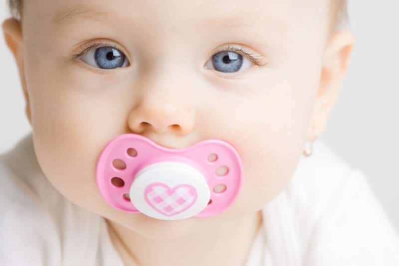 adorable baby girl with blue eyes sucking her pink pacifier
