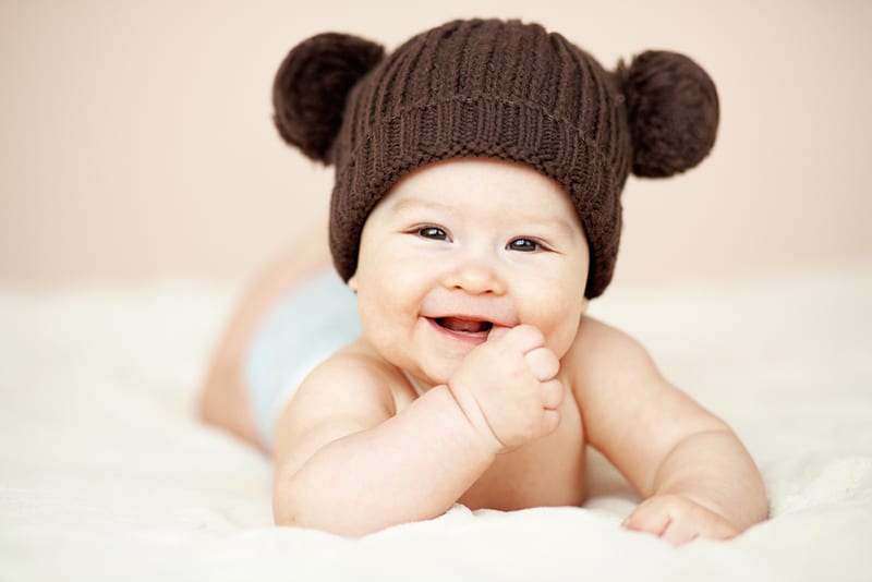 adorable baby wearing a teddy hat and smiling while lying on tummy