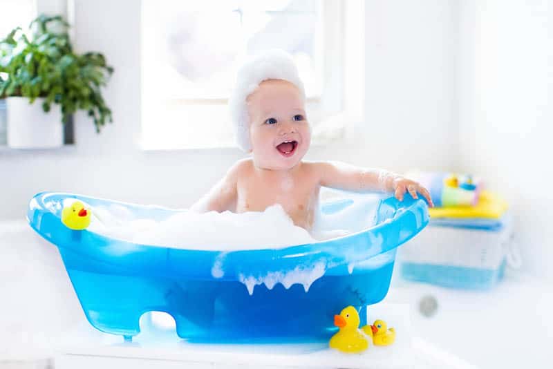 adorable happy baby taking a bath and playing with bubble foam and duck toys