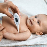 mother measuring baby's temperature with thermometer
