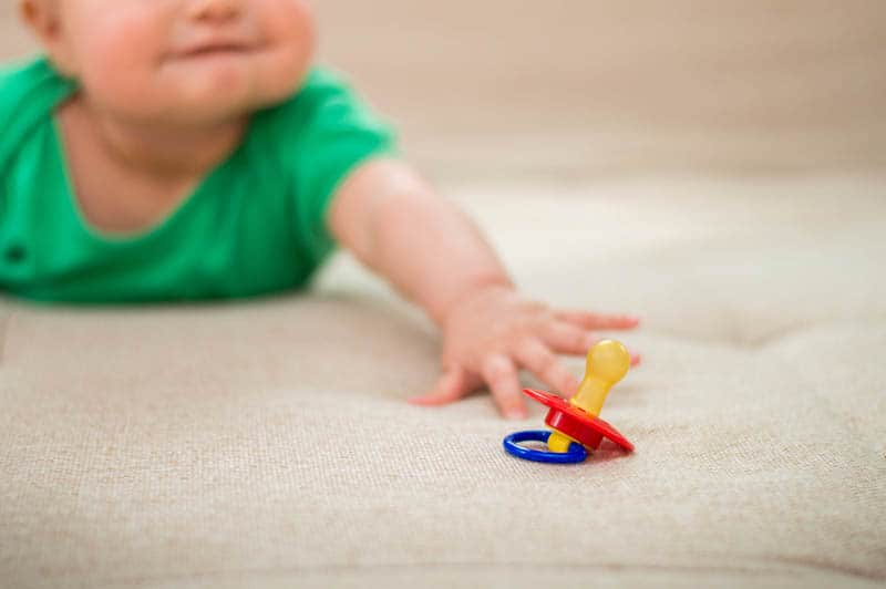 baby lying on belly and trying to reach a colorful pacifier on the floor