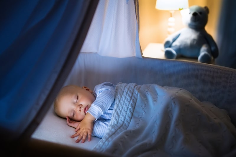 baby sleeping in a blue bassinet at night covered with blanket