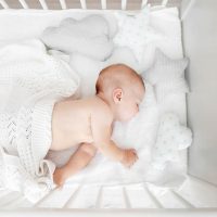 cute baby sleeping in a crib covered with a white blanket