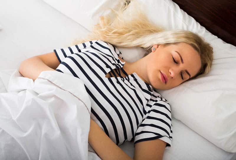 blond woman taking a nap in the bed covered with white sheet