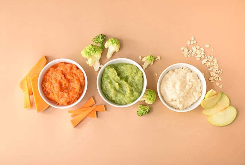 bowls with healthy baby food and vegetables on the orange table