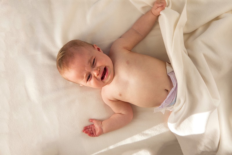 crying baby wearing diapers and lying on bed in white sheets