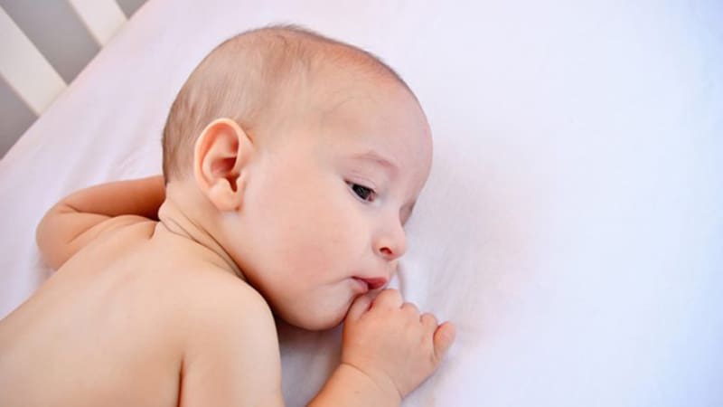 cute baby boy lying on bed and sucking his lower lip