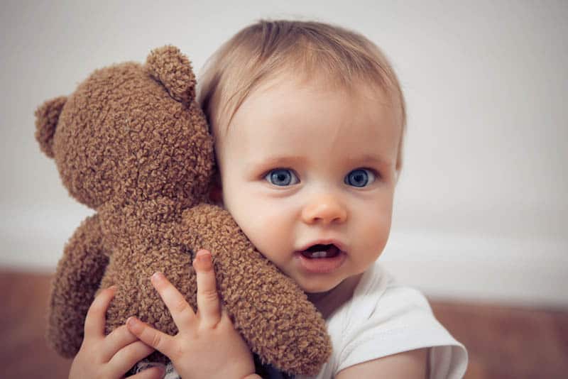 cute baby girl with blue eyes cuddling with teddy bear
