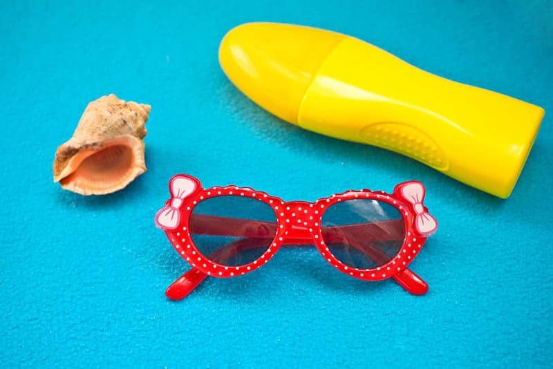 cute baby glasses with sunscreen and a shell on a blue towel