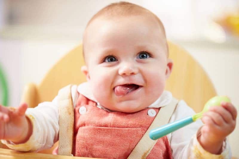 cute baby sitting in a high chair with spoon for eating