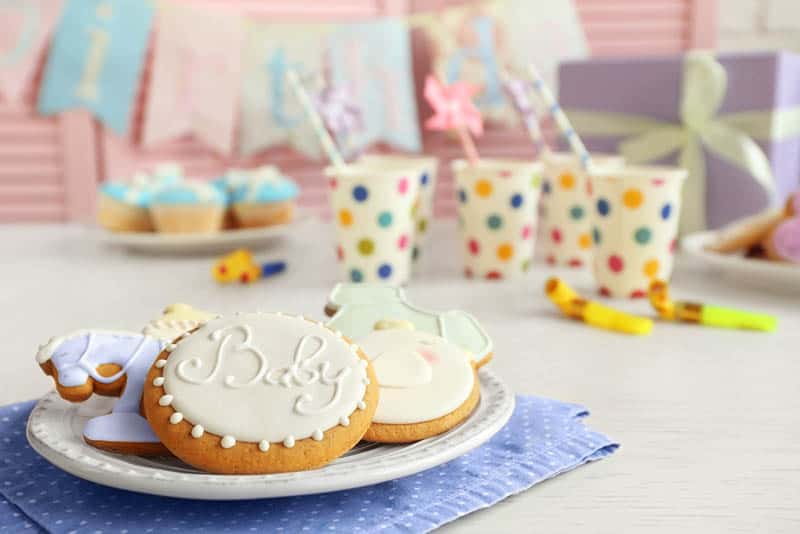 glazed cookies on the plate with glasses and decorations on the table for baby shower