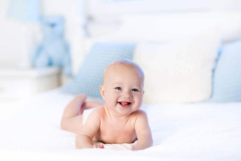 happy baby boy lying on belly on the bed and smiling