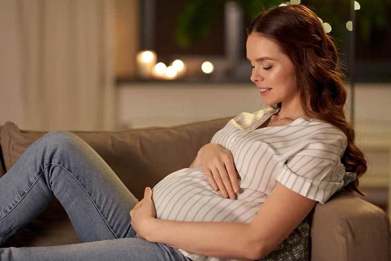 happy pregnant woman lying on the couch and caressing her belly
