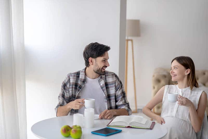 happy pregnant woman talking with her husband by the table at home