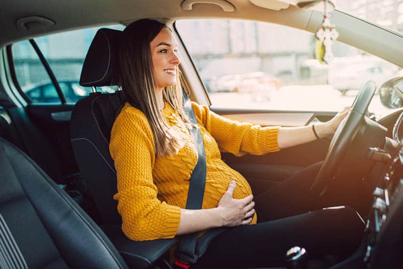 happy pregnant woman with safety belt driving a car