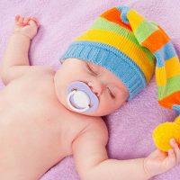 cute baby with colorful hat and a pacifier sleeping on the bed
