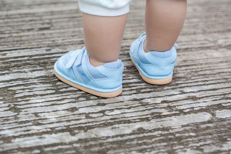 little baby walking in blue shoes on wooden floor