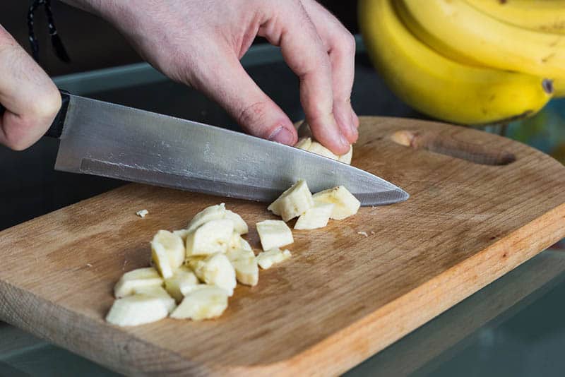 man cutting banana into the small pieces on the wooden board