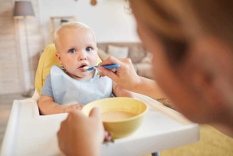mother feeding cute blond baby staring at her