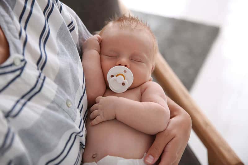 mother holding cute sleeping baby with pacifier in mouth