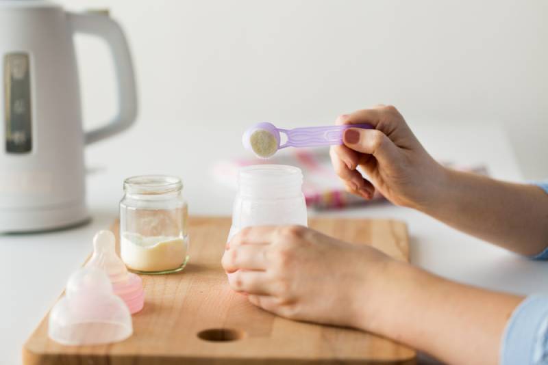 mother putting a baby formula with spoon into the baby bottle