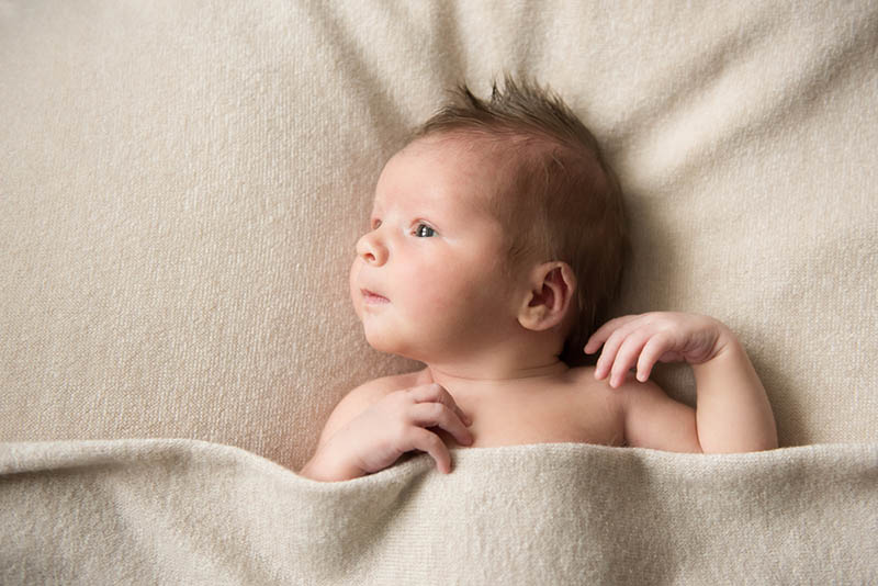 newborn baby lying on the bed covered with blanket and looking at distance