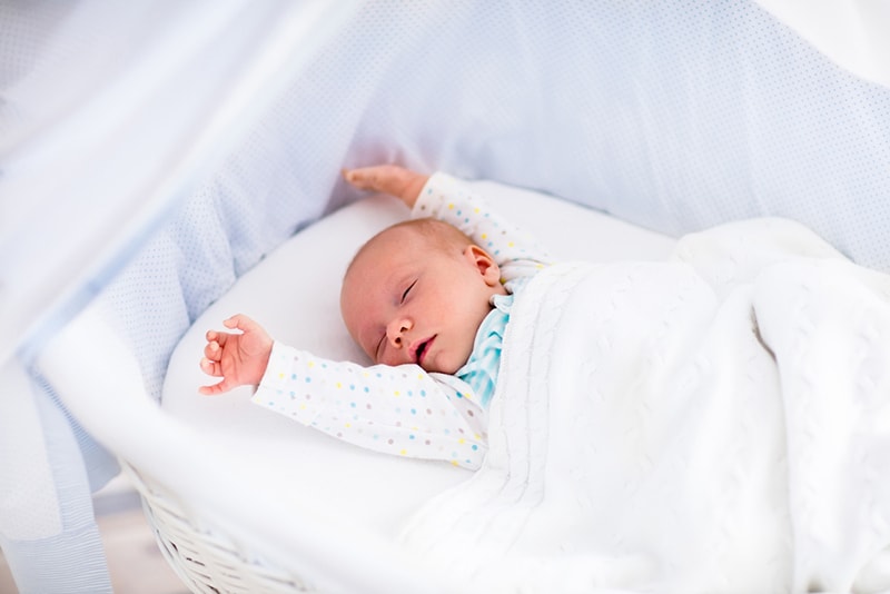 newborn baby with hands up sleeping in white bassinet