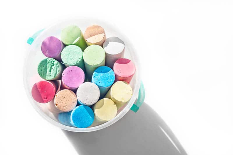 pack of sidewalk chalks in a plastic bucket on the white table with shadow