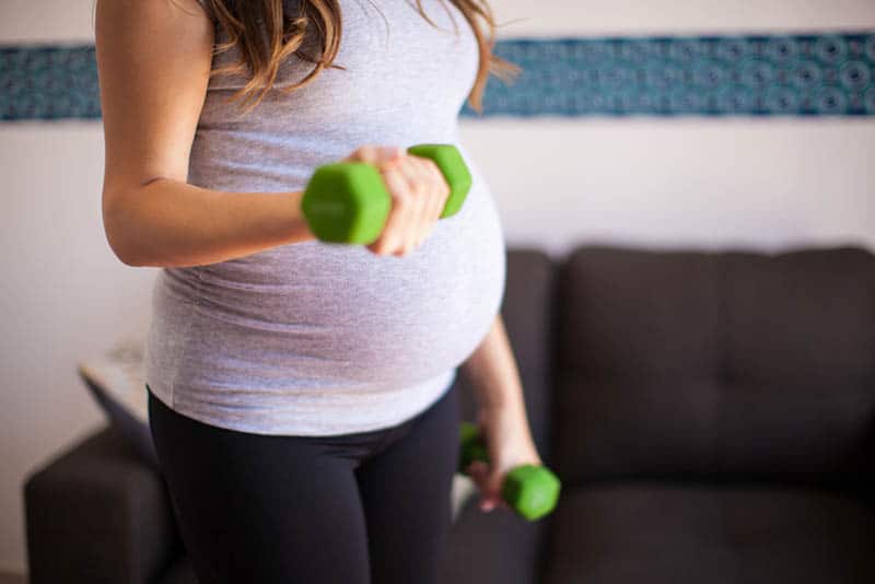 pregnant woman exercising at home with green dumbbells